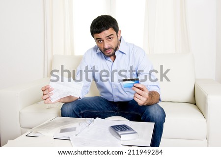 young attractive latin american business man at home sitting on sofa with credit card and calculator accounting costs, charges, taxes and mortgage for paying bills looking worried and stressed