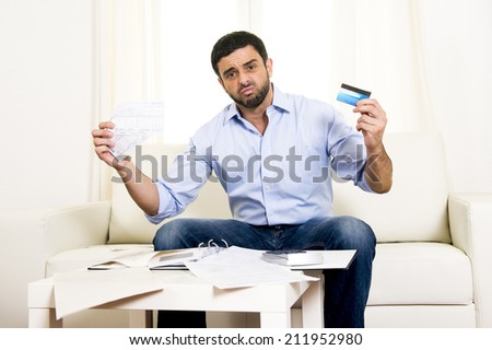 young attractive latin american business man at home sitting on sofa in stress with credit card and calculator accounting debts, bills and bank papers worried for money and financial situation
