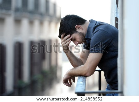 Lonely young man outside at house balcony looking depressed, destroyed, sad and suffering emotional crisis and grief thinking of taking a difficult and important life decision on an urban background