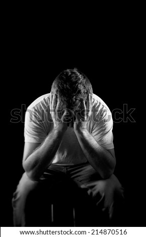 young wasted man with hands covering face suffering deep depression, pain, emotional disorder, grief and desperation concept isolated on black background with grunge studio lighting in black and white