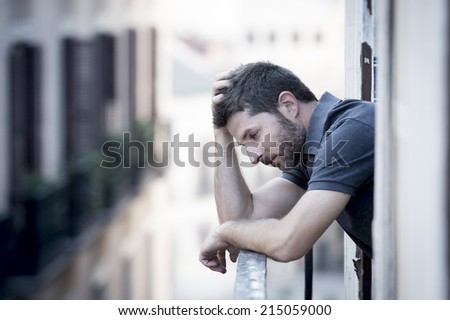 young man alone outside at house balcony terrace looking depressed, destroyed, wasted and sad suffering emotional crisis and depression on urban background