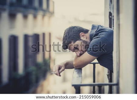 young man alone outside at house balcony terrace smoking depressed, destroyed, wasted and sad suffering emotional crisis and depression on urban background