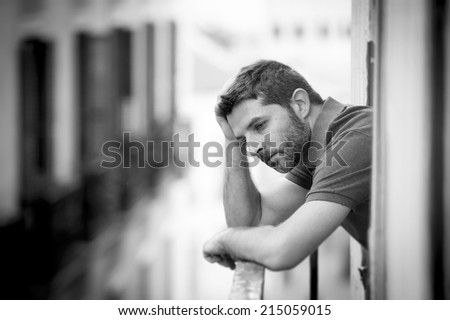 young man alone outside at house balcony terrace looking depressed, destroyed, wasted and sad suffering emotional crisis and depression on urban background in black and white