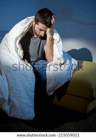 young sick man sitting on couch at home scary and desperate suffering insomnia, depression, nightmares, emotional crisis, mental disorder with a dim light and deep dark shadows