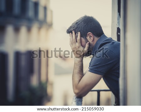 young man alone outside at house balcony terrace looking depressed, destroyed, wasted and sad suffering emotional crisis and depression on urban background