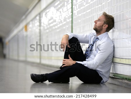 Young business man who lost job abandoned lost in depression sitting on ground street subway suffering emotional pain, thinking and leaning on wall alone