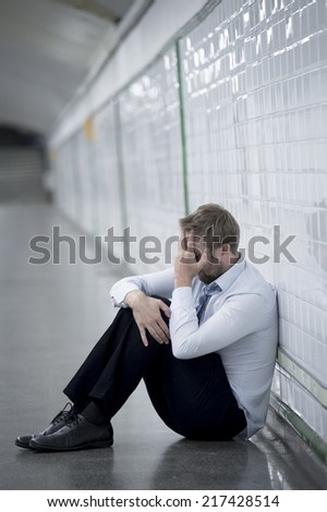 Young business man who lost job abandoned lost in depression sitting on ground street subway suffering emotional pain, thinking and leaning on wall alone