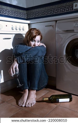 lonely drunk sick woman sitting on kitchen floor in depression feeling miserable holding his legs in barefoot looking desperate in alcoholism and drinking to forget concept