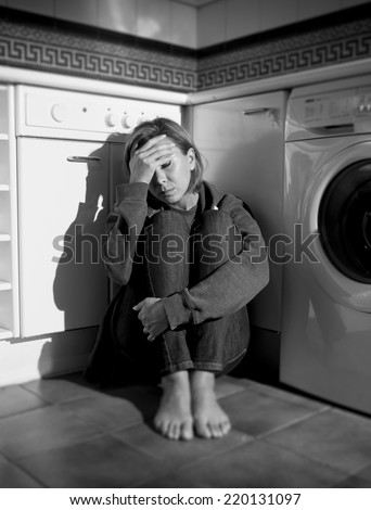 lonely depressed and sick woman sitting alone on kitchen floor in stress , depression and sadness feeling miserable in barefoot looking desperate in black and white vertical composition