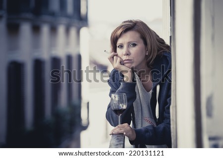 young attractive woman suffering depression smoking and drinking wine in stress outdoors at home balcony terrace window in pain and grief feeling sad and desperate in urban background