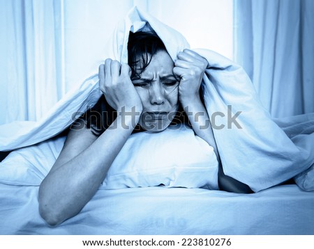 young moody woman in bed suffering stress with her insomnia problem and sleeping disorder or hangover covering with blanket and bedclothes on studio blue lighting