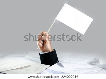 Hand of caucasian businessman emerging from office desk loaded of paperwork , invoices and a lot of papers and documents holding white flag  overworked in giving up concept