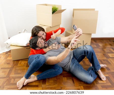 young happy couple moving together in a new house , flat or apartment unpacking cardboard boxes home belongings having fun taking selfie video and picture