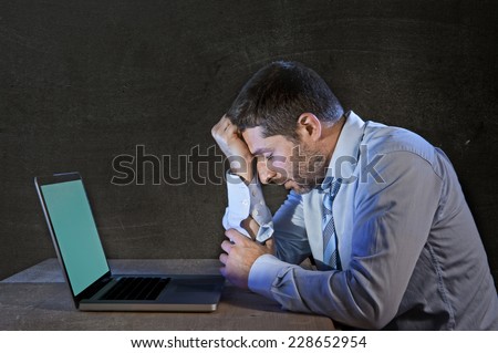 young stressed businessman working on desk with computer laptop thinking and looking sad and frustrated in depression and work problems concept isolated on black grunge background