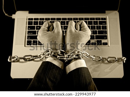 Hands of caucasian businessman addicted to work tied and bond with iron chain handcuffed to computer laptop in workaholic, internet slave and addict concept in black and white