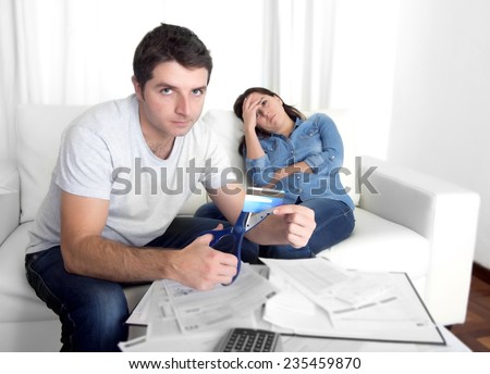 young couple fighting husband angry on bad financial situation cutting credit card with scissors woman trying to stop him in shopaholic wife accounting at home couch