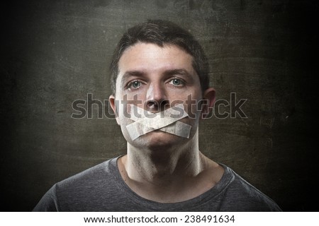 attractive young man with mouth sealed on duct tape to prevent him from speaking keeping him mute and censored in freedom of speech and expression concept isolated on dark grunge studio light style