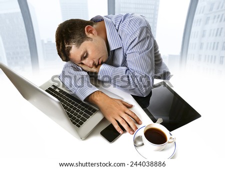 overworked businessman wearing blue shirt asleep at work tired and overloaded sitting with computer laptop, mobile phone and coffee cup in business district office