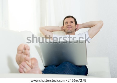 happy attractive Brazilian man freelance working with computer laptop laying on couch at home relaxed thinking and dreaming of future successful work project