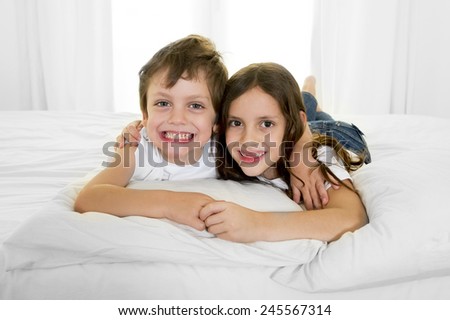 7 years old little girl posing on bed or couch together with her 4 years old small brother smiling happy in brotherhood and children lifestyle concept