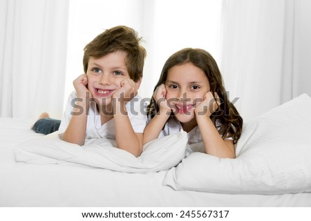 7 years old little girl posing on bed or couch together with her 4 years old small brother smiling happy in brotherhood and children lifestyle concept