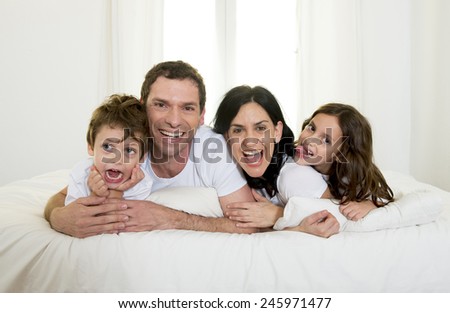 young happy Brazilian family playing together on bed with mother, father, daughter and son having fun smiling and laughing in bedroom in love and lifestyle concept