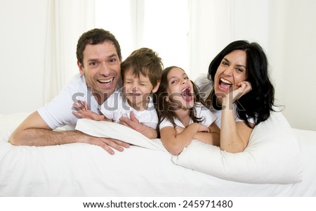 young happy Brazilian family playing together on bed with mother, father, daughter and son having fun smiling and laughing in bedroom in love and lifestyle concept