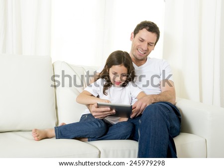 young attractive father sitting on couch with 7 years old sweet little girl daughter using digital tablet pad at home smiling happy together in children technology concept