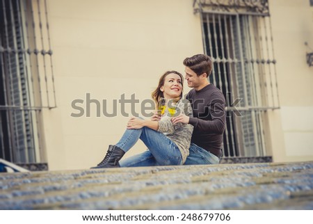 candid portrait of young beautiful couple in love sitting on street together celebrating Valentines day with Champagne toast on casual clothes and urban background