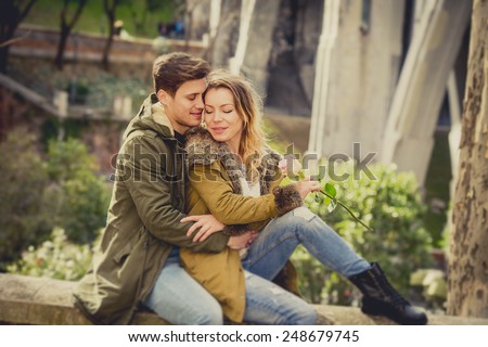 candid portrait of young beautiful couple in love sitting on street together celebrating Valentines day with rose casual winter clothes and urban background