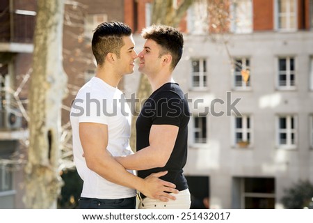 young happy attractive gay men couple cuddling and kissing outdoors on street in sexual freedom and free homosexual love concept in urban background