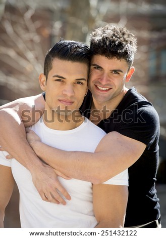 young happy attractive gay men couple with strong fit body cuddling posing outdoors on street in sexual freedom and free homosexual love concept in urban background