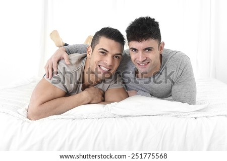 young attractive gay men couple lying on bed together in bedroom smiling happy in love wearing casual clothes in homosexual relationship concept