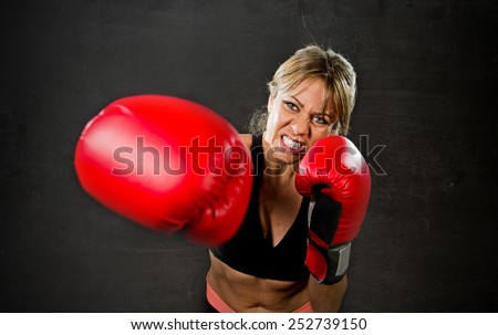 young fit and strong sexy boxer girl with red boxing gloves fighting throwing aggressive punch training workout in gym feeling angry isolated on black background