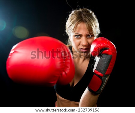 young fit and strong sexy boxer girl with red boxing gloves fighting throwing aggressive punch training workout in gym feeling angry isolated on black background