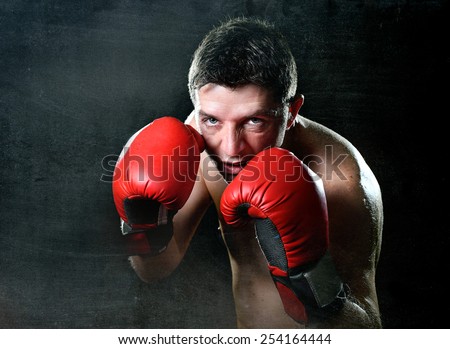 young man training shadow boxing with red fighting gloves posing in boxer stance with angry rage face expression isolated on black grunge dirty background