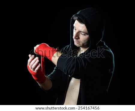 young man in boxing hoodie jumper with hood on head wrapping hands and wrists getting ready for fighting posing concentrated isolated on black  background
