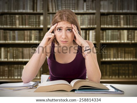 young beautiful college student girl studying busy for university exam worried desperate and in stress feeling tired and test pressure sitting on desk with book in youth education concept