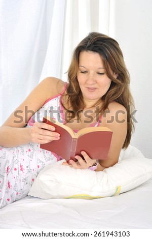 young attractive and beautiful woman in nightgown lying on bed at bedroom reading novel book in relax looking tranquil and happy in American lifestyle concept