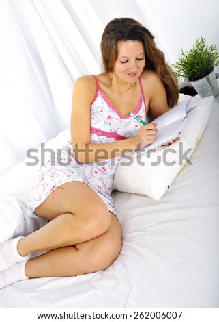 young attractive and beautiful woman in nightgown lying on bed at bedroom writing diary with pen in relax looking tranquil and happy in American lifestyle concept