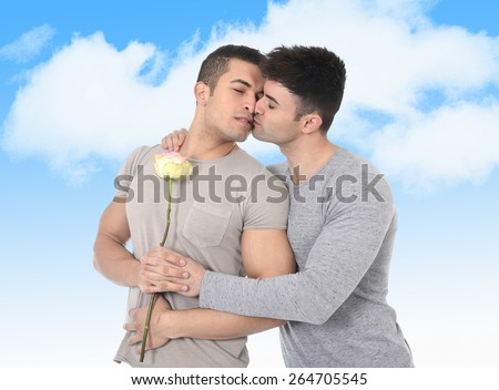 attractive gay couple of homosexual young men strong fit bodies celebrating anniversary love together kissing on valentines day with rose flower isolated on blue sky background