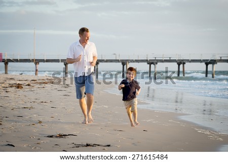 young happy father playing on the beach with little son running excited with barefoot in sand and water, the kid smiling and having fun together with dad in Summer vacation concept