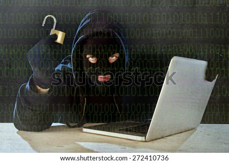 hacker man in black hood and mask with computer laptop holding lock in dangerous dark look hacking system having access to data info and privacy in business digital crack and cyber crime concept