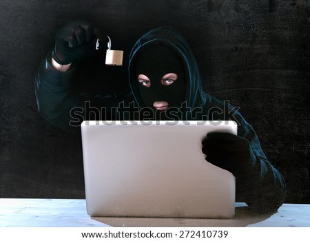 hacker man in black hood and mask with computer laptop holding lock in dangerous dark look hacking system having access to data info and privacy in business digital crack and cyber crime concept