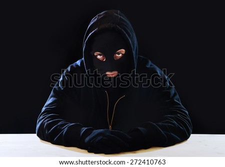criminal or terrorist man in gloves, black hood and thief mask looking dangerous with hidden identity in secret illegal activity and crime concept with creepy scary terrorist and maniac look