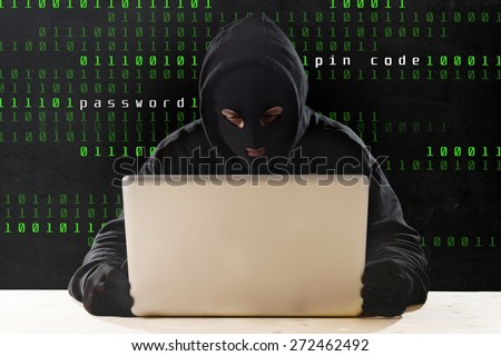 hacker man in black hood and mask with computer laptop and dangerous dark look hacking system having access to data info and privacy in business digital cybercrime or cyber crime concept