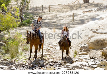 young American Australian man as father or horse instructor of young girl or  teen daughter riding little pony wearing cowgirl hat in countryside Summer vacation ride