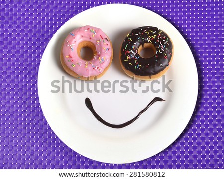 smiley happy face made on dish with donuts as eyes and chocolate syrup as smile in sugar and sweet addiction and nutrition concept on purple mat
