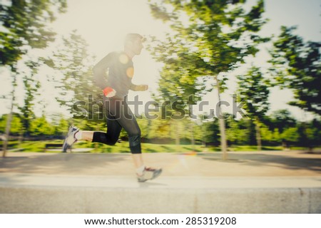 motion blur image of young man running practicing sport in city park with extreme backlight lens flare lighting effect in fitness and healthy lifestyle concept