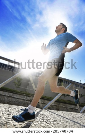 extreme sun back light on young athletic man practicing running in urban background with lens flare on a blue sky in fitness , body care, sport training and healthy lifestyle concept